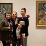 Three students posed in front of art work