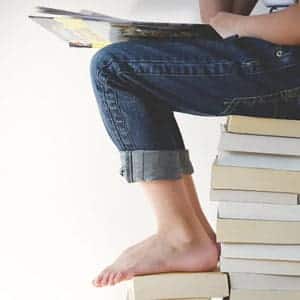 student sitting on stack of books