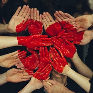 multiple hands together painted with a red heart