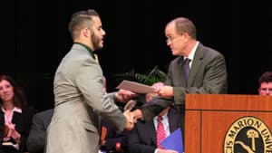 Dr. Chris Johnson hands student certificate on stage at podium