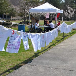 Clothesline hung with decorated shirts and tent in background on campus