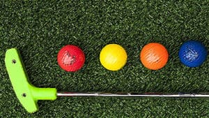 putter on artificial grass with red, yellow, orange and blue balls