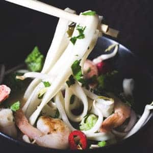 black bowl of shrimp, noodles and seasonings eaten with chopsticks