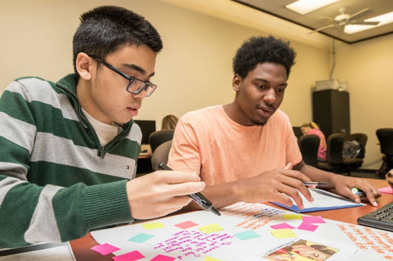 Two students make notes on a posterboard.