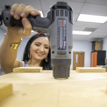 FMU 2019 graduate Taylor Watson sits in an Industrial Engineering lab with a drill.