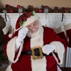 Santa Clause sits in front of a fireplace.