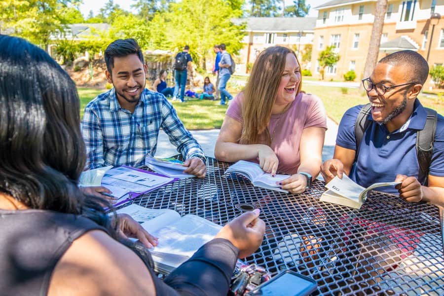 Four FMU students sit at a table on a sunny day.