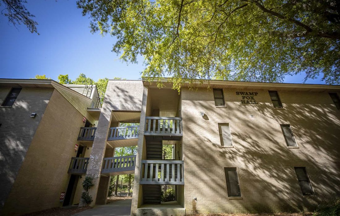 Sun shines through the trees onto Swamp Fox Hall.