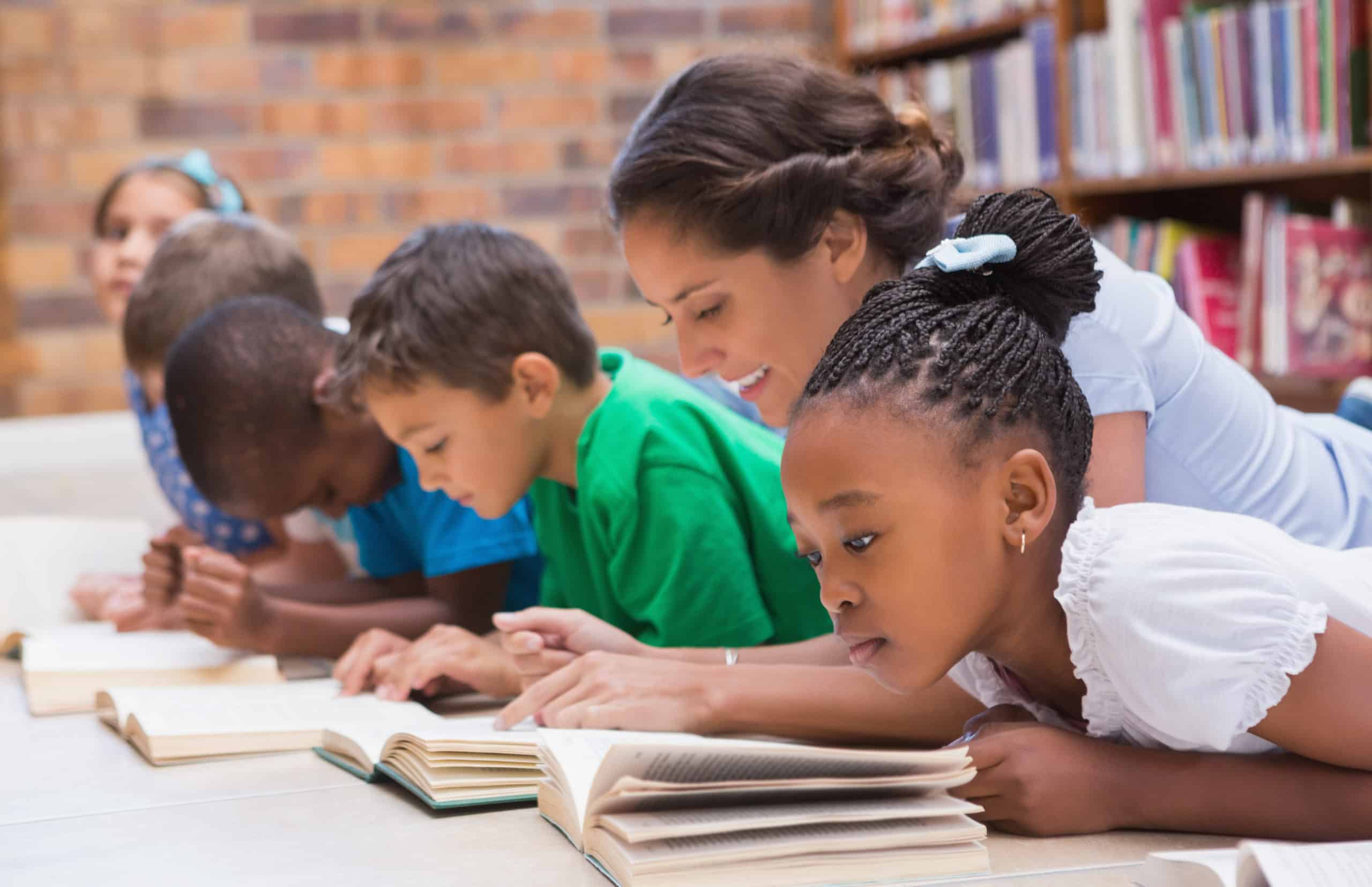 Cute,Pupils,And,Teacher,Lying,On,Floor,In,Library,At