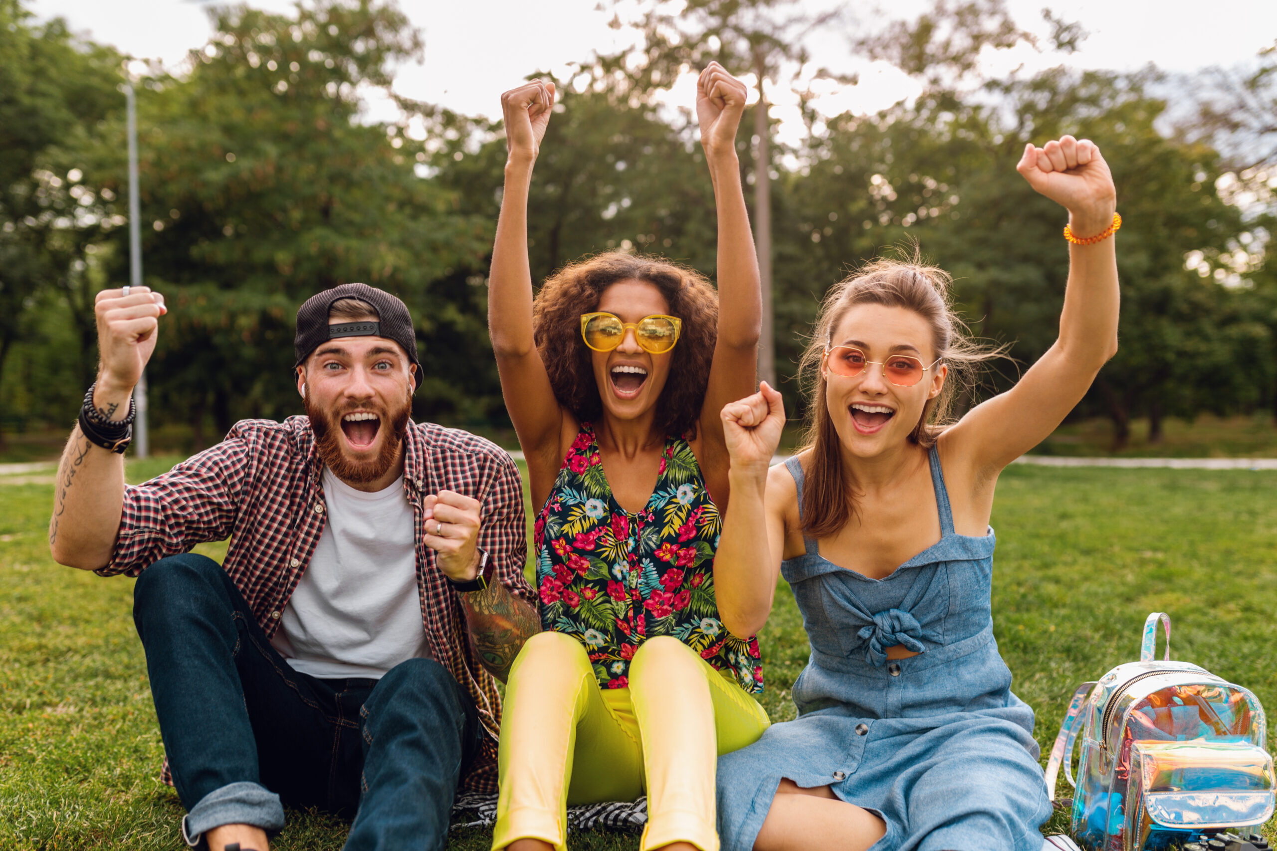 happy young company of smiling friends sitting park on grass, man and women having fun together, colorful summer hipster fashion style, traveling sightseeing